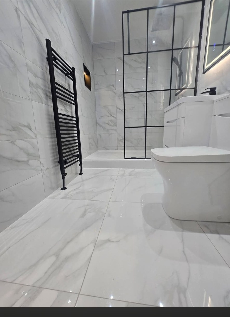 White marble tiled bathroom with black towel rail and walk-in shower