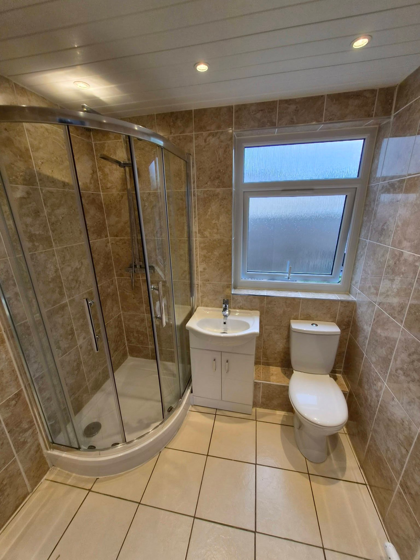Brown travertine tiled bathroom with quadrant shower and small vanity before refit
