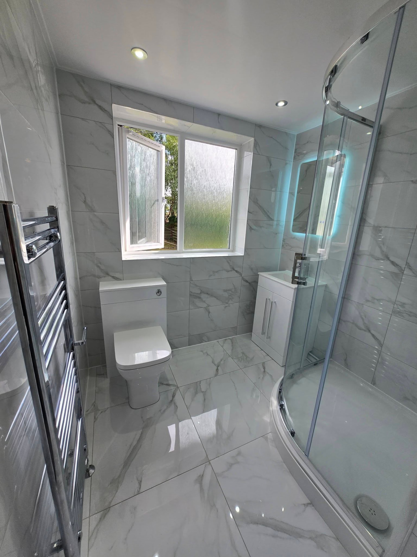 Marble-tiled bathroom with quadrant shower enclosure, LED mirror and chrome towel rail after refit