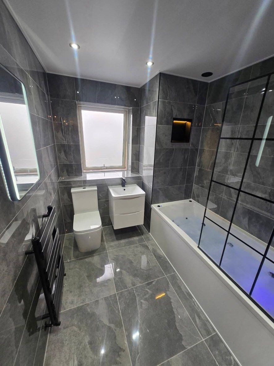 Grey tiled bathroom with LED mirror, black towel rail and lit bath