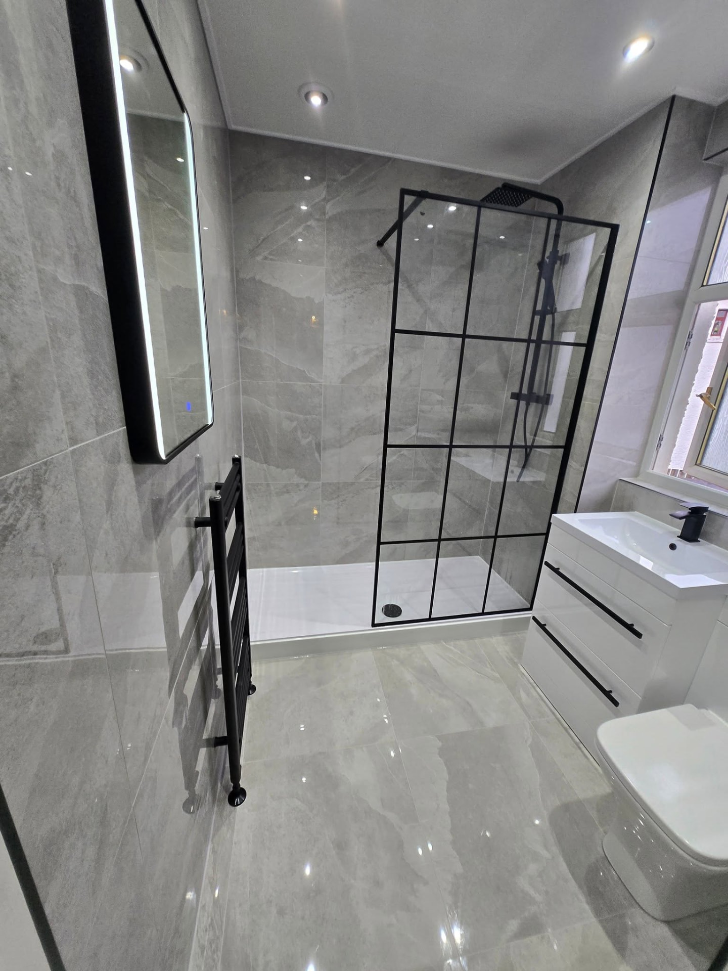 Grey stone-effect bathroom with black-framed walk-in shower, LED mirror and gloss vanity after refit