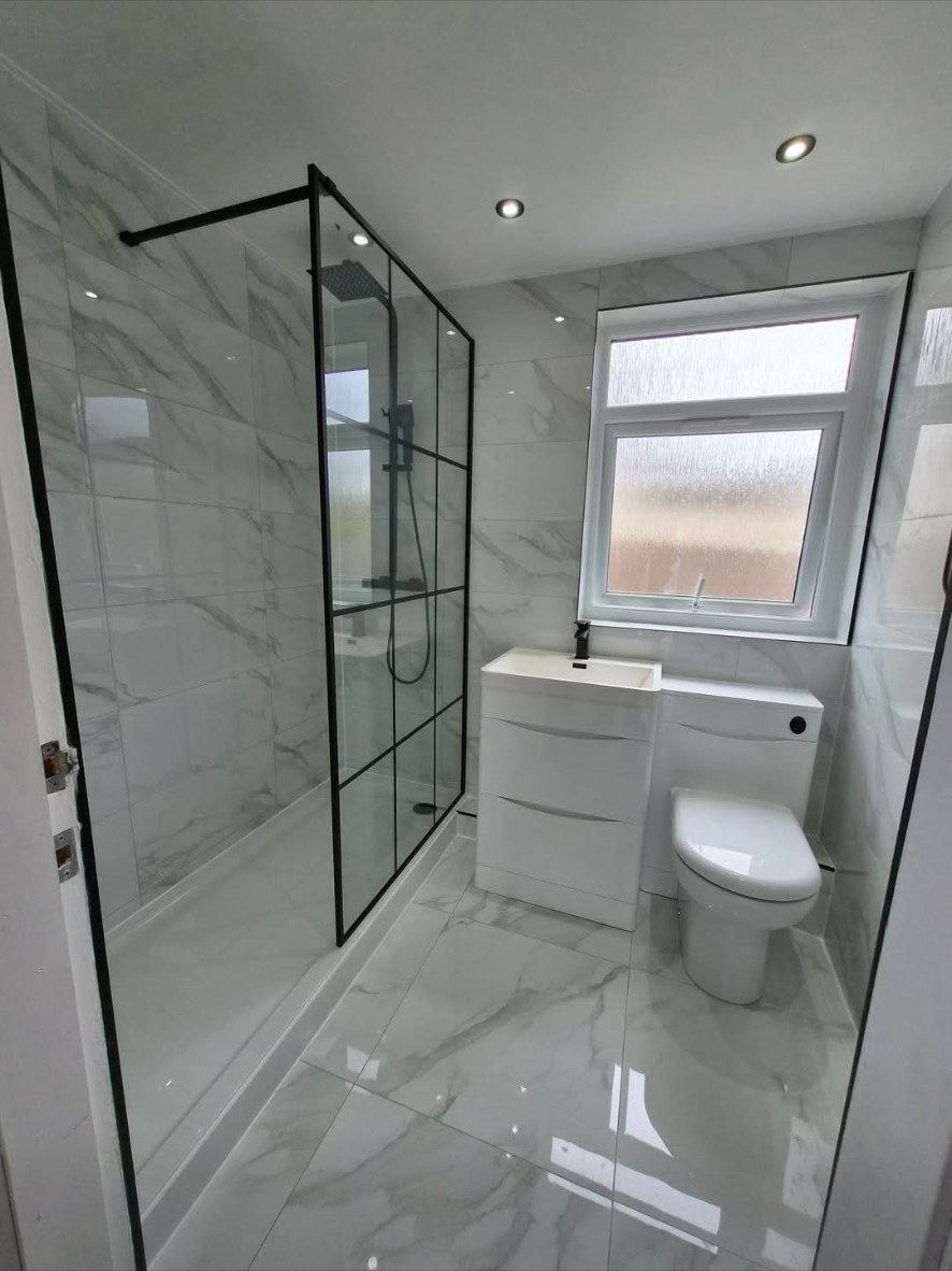 Marble-tiled bathroom with black-framed walk-in shower and white vanity