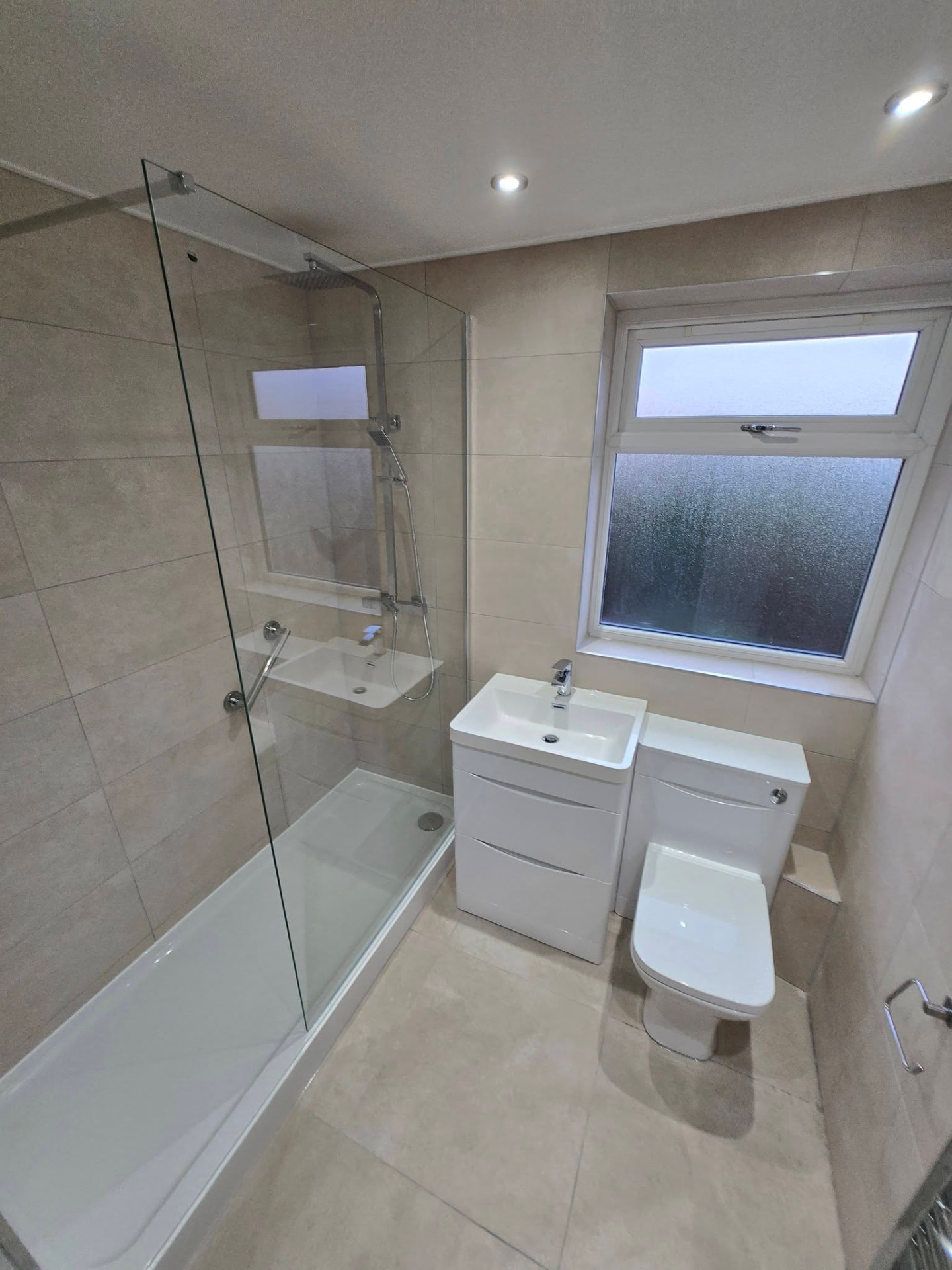 Finished bathroom with stone-effect tiling, bath with glass screen, vanity unit and back-to-wall WC