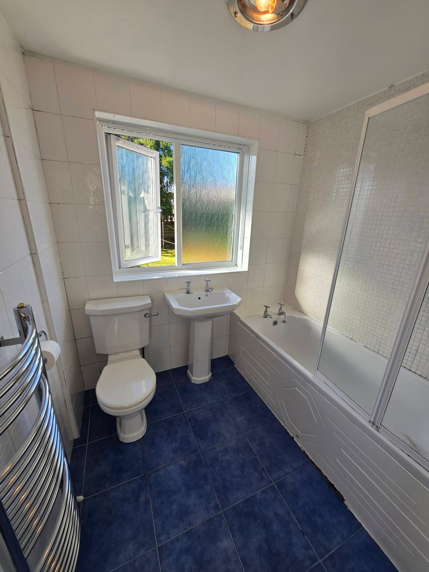Old bathroom with white tiles, blue floor tiles and bath with shower screen before refit