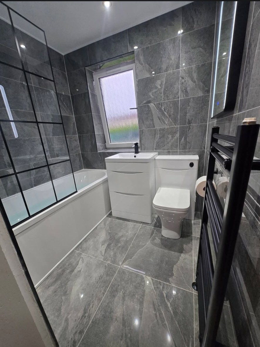 Grey stone-effect tiled bathroom with black bath screen and white vanity unit