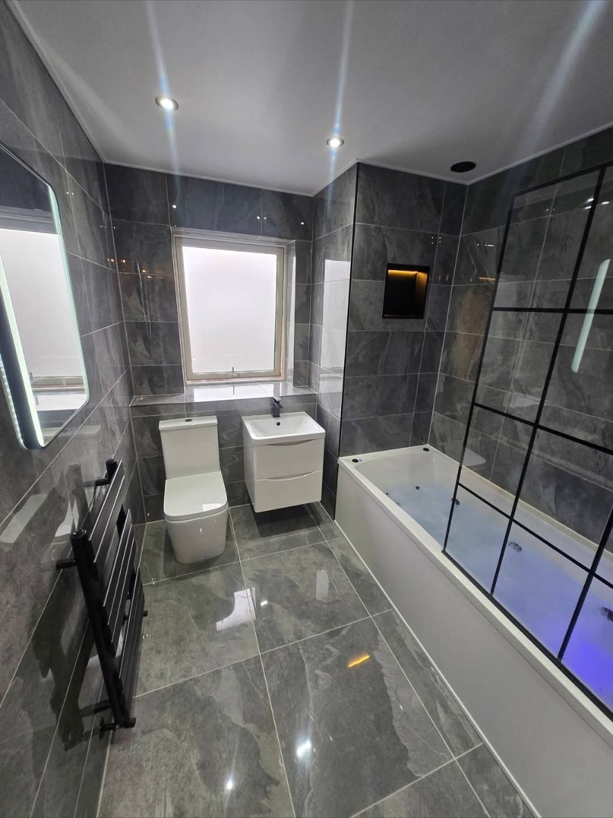 Dark grey stone-effect bathroom with LED mirror and lit bath