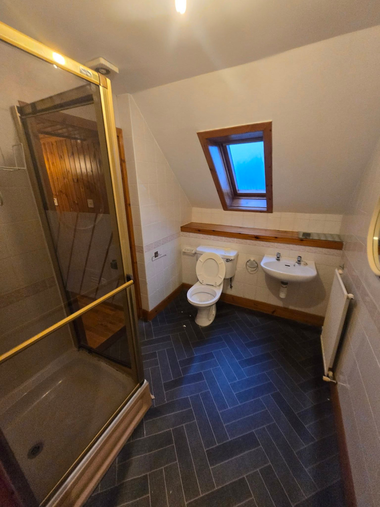 Attic bathroom with gold-framed shower enclosure and dark herringbone floor before refit