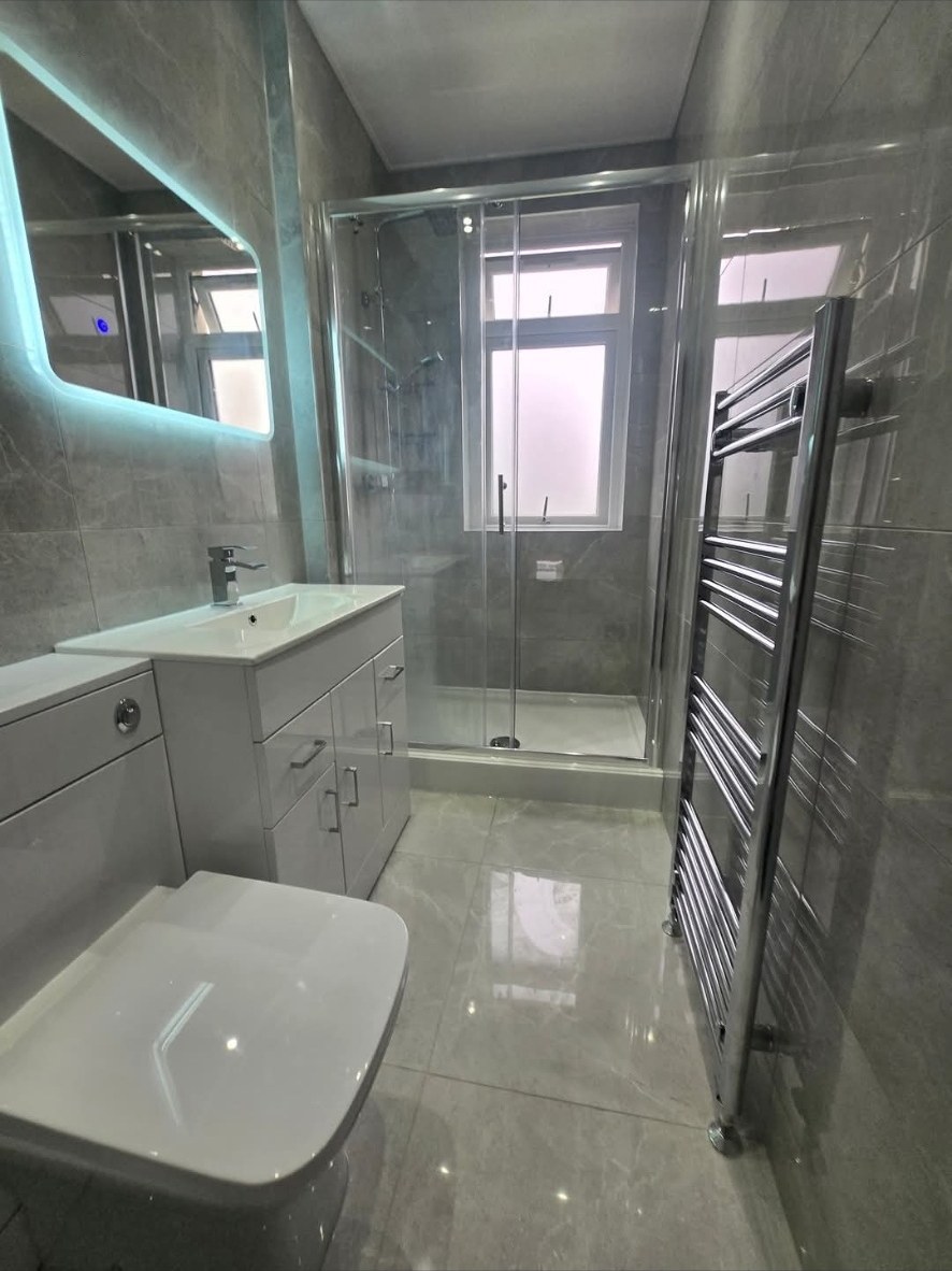 Grey tiled bathroom with sliding-door shower enclosure and chrome towel rail