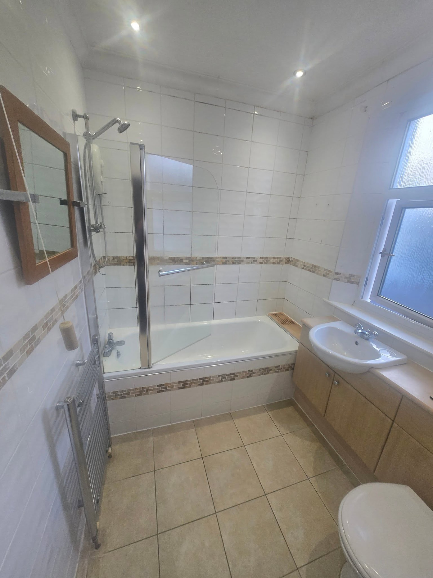 Old white tiled bathroom with bath, mosaic border and wooden vanity before refit