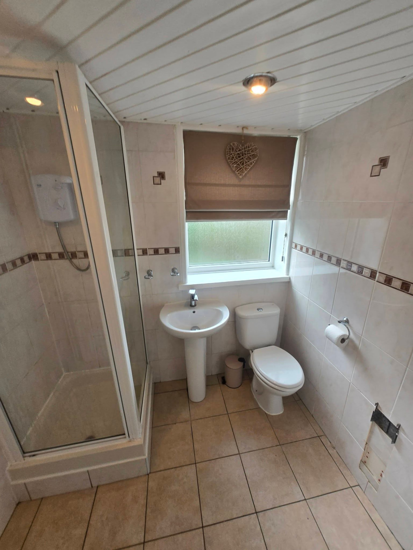 Old bathroom with pedestal basin, corner shower enclosure and beige border tiling before refit