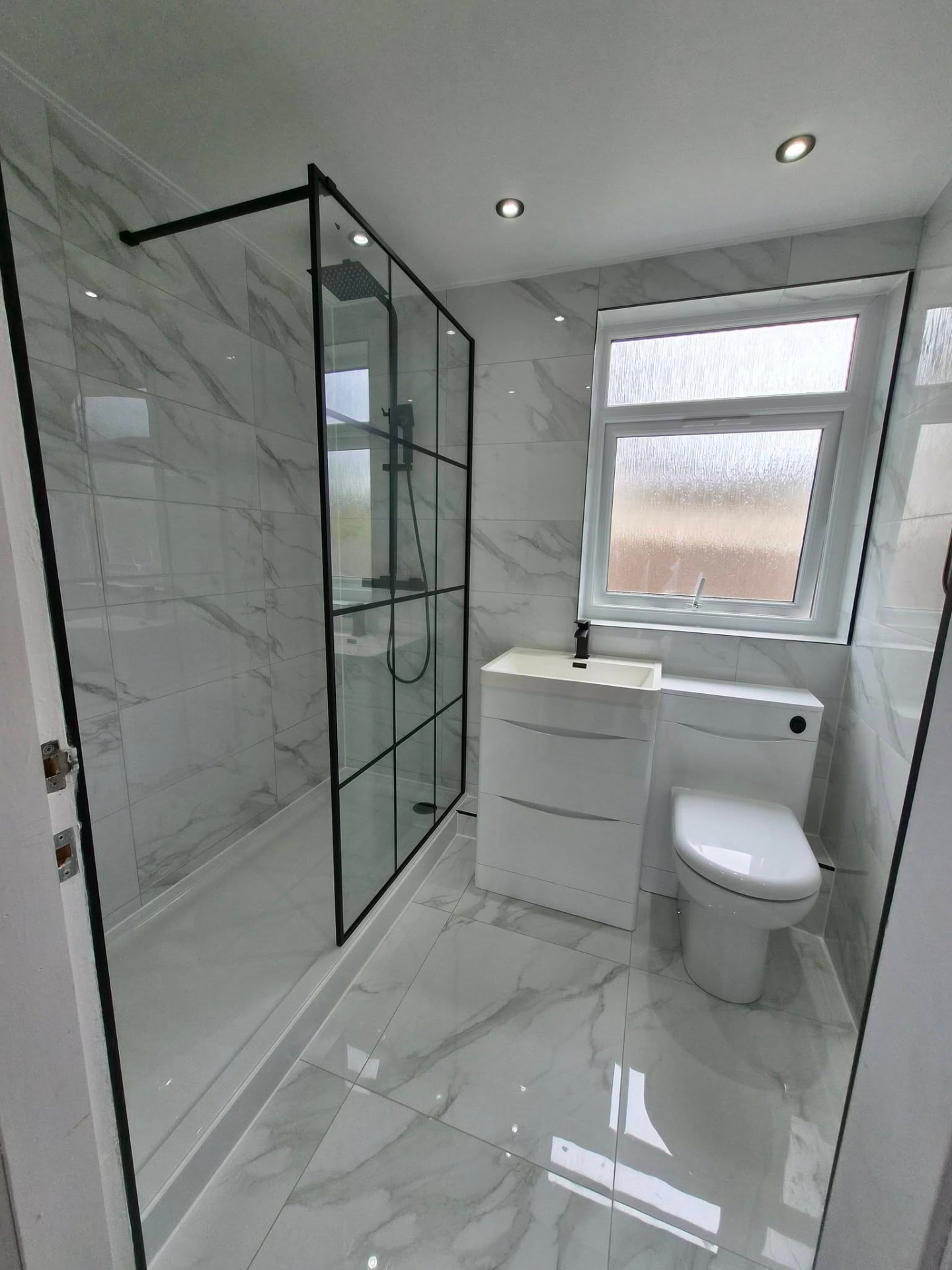 White marble bathroom with black-framed walk-in shower, vanity basin and WC unit after refit