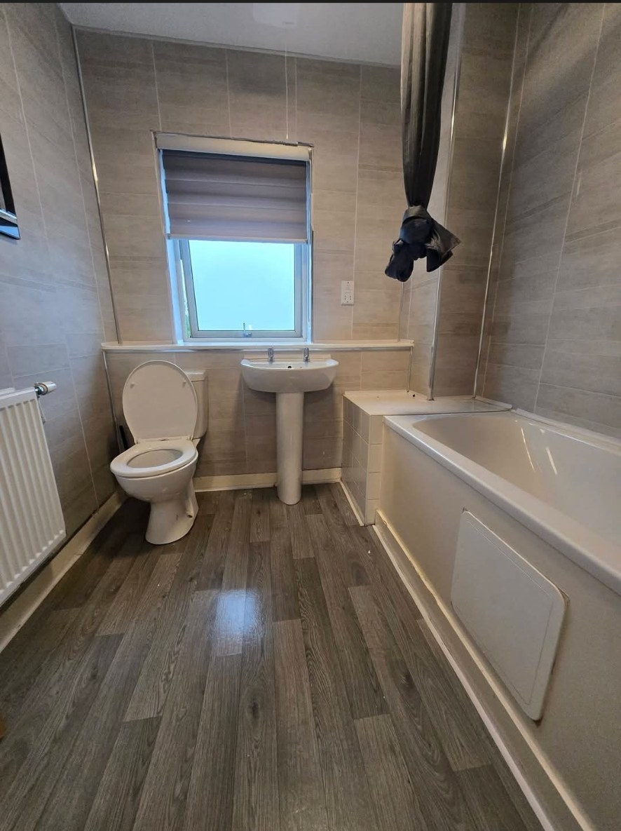 Beige tiled bathroom with wood-effect floor before refit