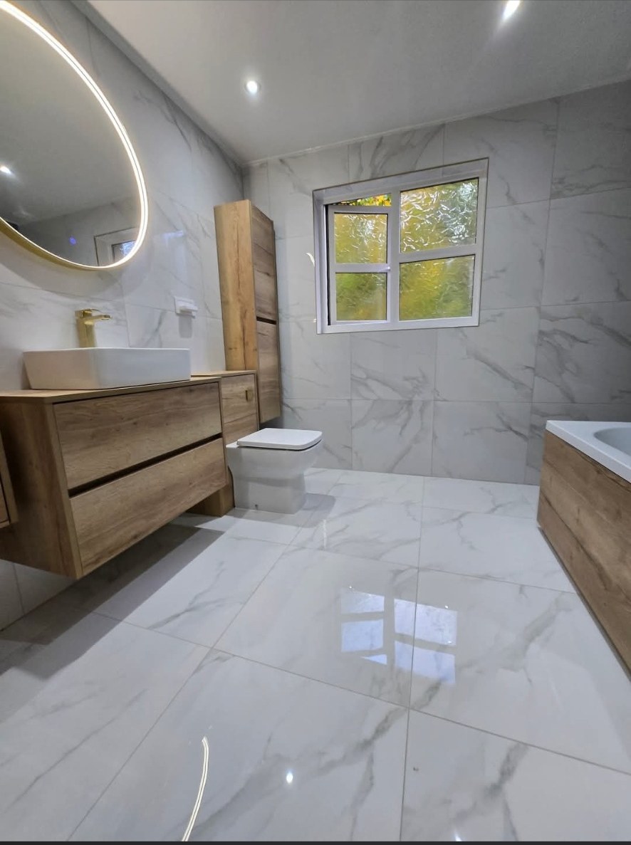 Marble bathroom with oak vanity unit and gold circular LED mirror
